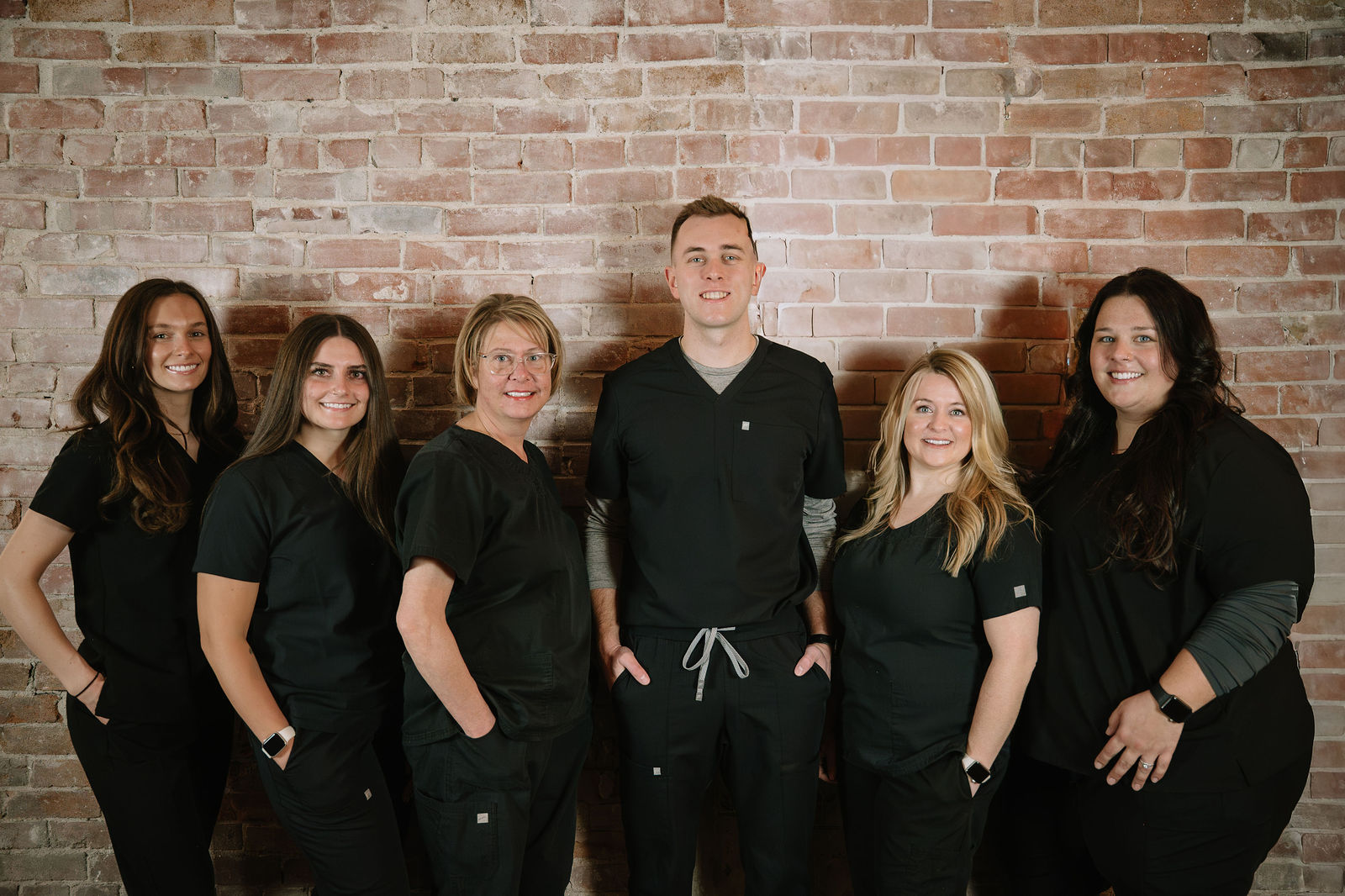 The Earlham Family Dentistry team in black scrubs against their warm exposed-brick wall